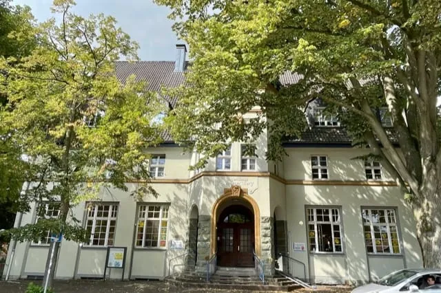 Das ehemalige Jugendhaus heute: hell verputztes Gebäude mit Rundbogenportal zwischen Bäumen.